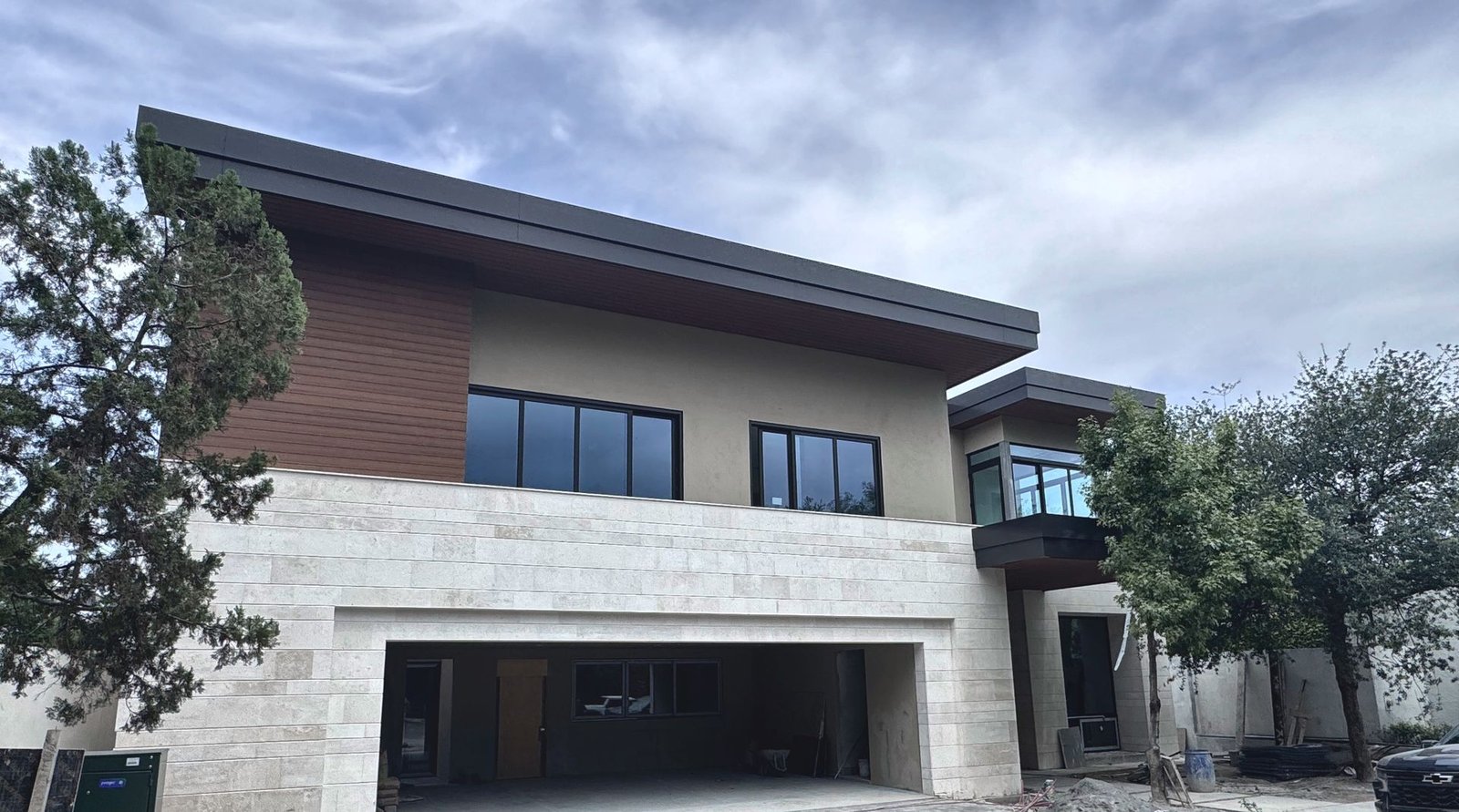 Fachada de una residencia moderna en San Pedro Garza García, con ventanería de PVC negro, recubrimiento de travertino y madera