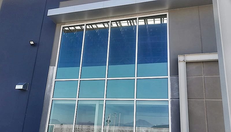 Ventanal de gran altura con cristal azul que refleja la sierra, en una obra industrial de Monterrey